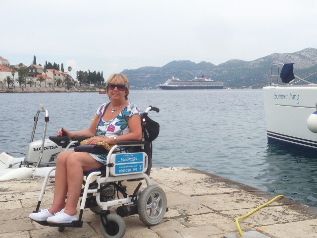 Customer smiling for the camera while using a powerchair, with cruise ship in background.